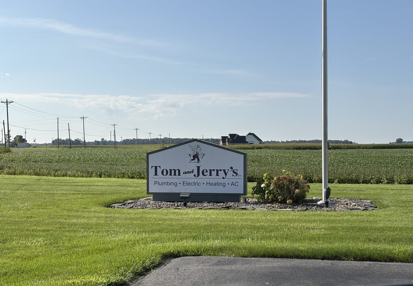 The Tom & Jerry's sign at the shop entrance on Dawson Road, with farm fields behind it