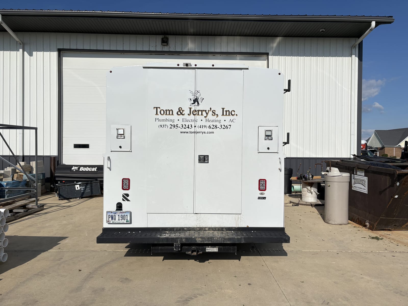 The back of a Tom & Jerry's service truck, lettered Plumbing, Electric, Heating and AC with both phone numbers