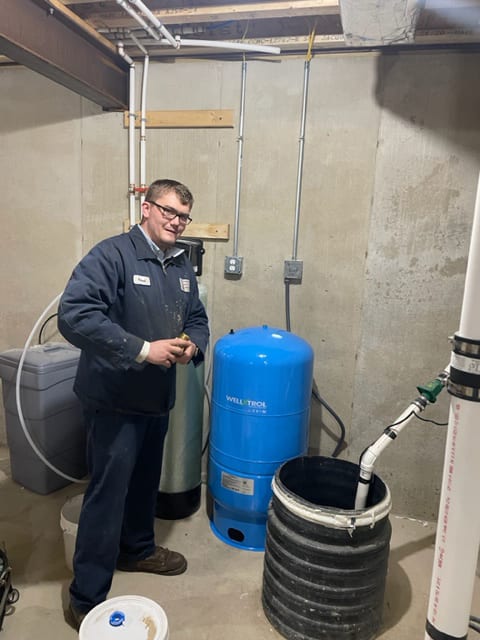 A Tom & Jerry's plumber beside a Well-Trol pressure tank and water softener in a basement